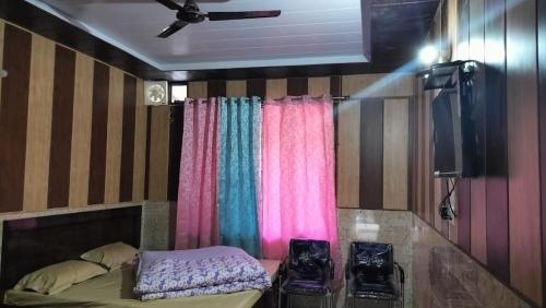 a room with a bed and a tv and curtains at Hotel Akshat in Barkot