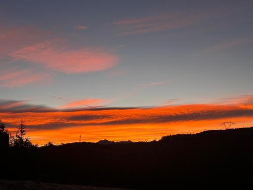a sunset in the sky with trees and mountains at Gîte Belle Vue 2 in Saint-Léger-les-Mélèzes