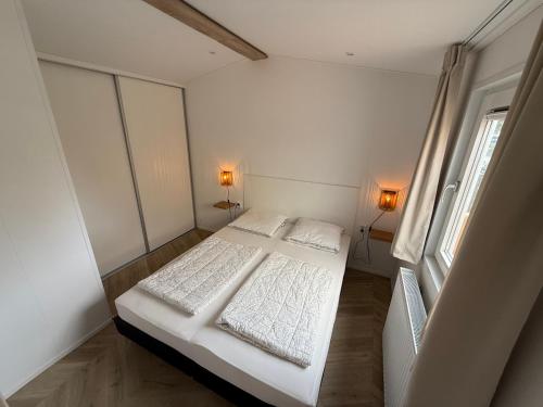 a bedroom with a bed with white sheets and a window at Luxe chalet op 5-sterren camping met comfortabel ingerichte veranda - parkkosten zijn inbegrepen in Sevenum