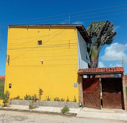 a yellow building with a palm tree next to it at Pousada da Sami in Barra de São Miguel