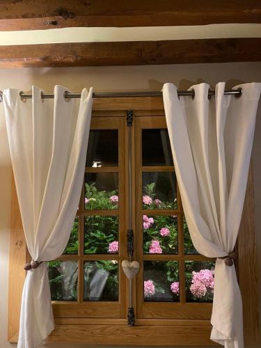 une fenêtre avec des rideaux blancs devant des fleurs dans l'établissement La Moutinière, luxury cottage with pool, à Manerbe