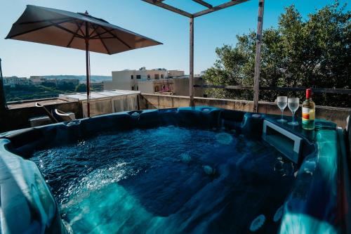 a plunge pool with an umbrella and wine glasses at Mohba Townhouse, Private Roof Top Jacuzzi, Garden, BBQ by Haven & Keys Malta in Xagħra