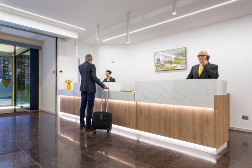 a man with a suitcase standing at a reception desk at Victor Hotel in Bari