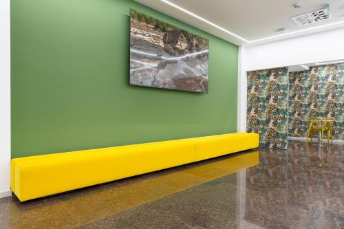 a yellow bench against a green wall with a painting at Victor Hotel in Bari
