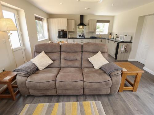 a living room with a brown couch and a kitchen at The Old Stables in Oasby