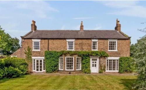 a large brick house with white doors and ivy at Hutton Mount Retreats in Ripon