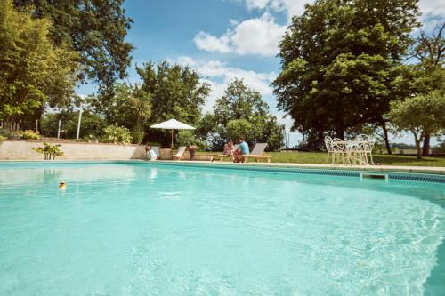 a large swimming pool with people sitting in a yard at La Ferme de Jeanne in Francescas