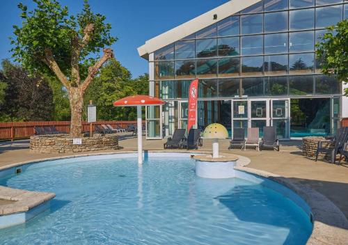 a pool with an umbrella in front of a building at Camping Le Ty Nadan - Eurocamp I Homair in Locunolé