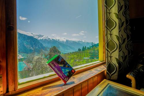a book sitting on a window sill with a view at 4 Bedroom Luxury Bungalow In Manali With Beautiful Scenic Mountain & Orchard View - #Private Bungalow #Premium Big rooms #Parking #Guest Preferred in Manāli