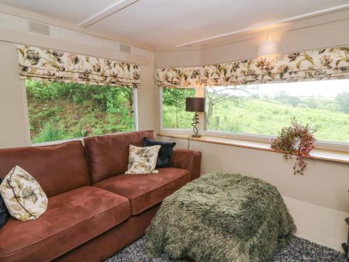 a living room with a brown couch and two windows at Gwybedog in Llanwrda