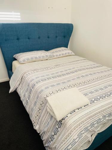 a bed with a blue headboard and a white blanket at Cozy and Peaceful home surrounding by cafes and restaurants in Perth
