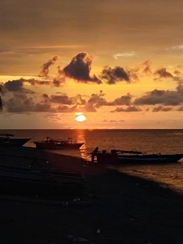 a sunset on the beach with boats in the water at Kahyangan hotel in Dondo