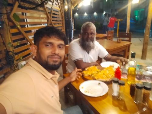 Dos hombres sentados en una mesa con un plato de comida. en Hotel jem, en Nikawatawana