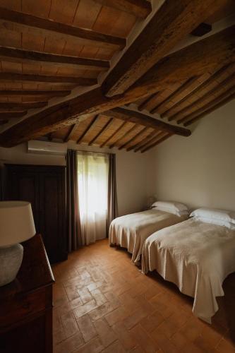 two beds in a room with wooden ceilings and a window at Podere la Piscina RestArt in San Casciano dei Bagni
