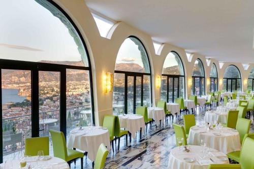 a restaurant with white tables and green chairs and windows at Grand Hotel President in Sorrento