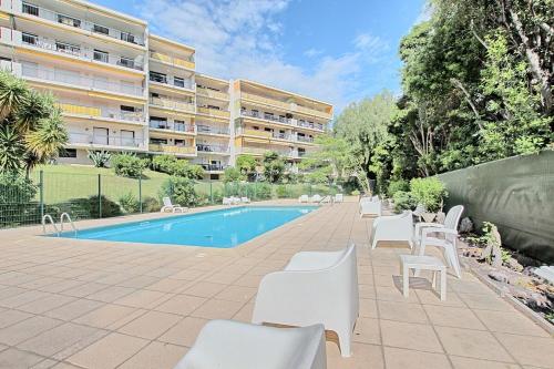 une piscine avec des chaises blanches et un bâtiment dans l'établissement Appartement proche Port et plages, à Antibes