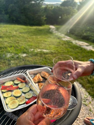 a person holding two glasses of wine next to a grill at Szarvas Vendégház in Zebegény