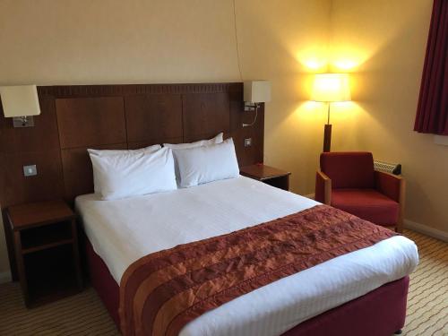 a hotel room with a large bed and a red chair at Holiday Inn Northampton by IHG in Northampton