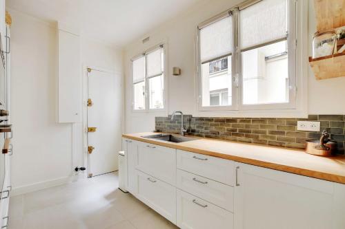La cuisine est équipée de placards blancs, d'un évier et de fenêtres. dans l'établissement Elegant Apt 2BDR Arc de Triomphe Champs-Élysées, à Paris
