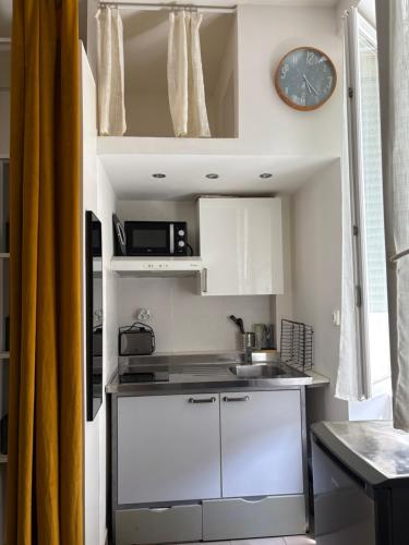 une petite cuisine avec des placards blancs et une horloge murale dans l'établissement Charmant studio en centre-ville, à Ajaccio