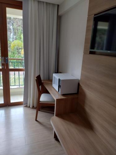 a room with a desk with a microwave and a window at Vista Azul Apart Hotel - Suítes com vista para a mata de pinheiros in Pedra Azul
