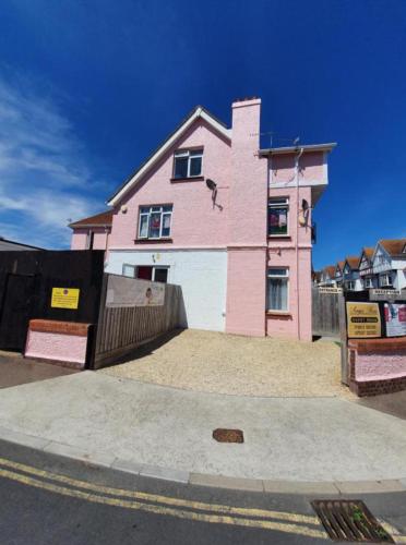 a pink house sitting on the side of a street at Paignton seafront Apartment with Private Garden ,FREE Private Car Space FREE WIFI ,No kitchen but Fridge Tea coffee Towels YES Double & Single bed YES Reception to help you YES Opposite the Beach Yes in Paignton