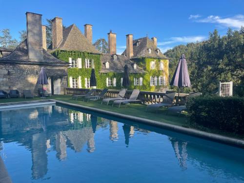 einem Pool mit Stühlen und Sonnenschirmen vor einem Gebäude in der Unterkunft Domaine de Carrière in Marvejols