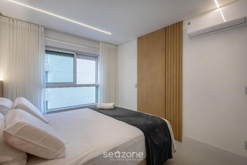 a bedroom with a white bed and a window at Condomínio a beira-mar c/ piscina - SHC in Piçarras