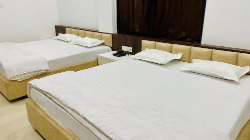 two beds in a hotel room with white sheets at Hotel Shree Rameshwaram in Godarpura