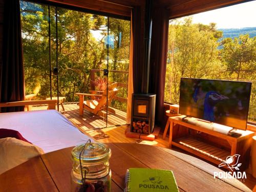a living room with a tv and a large window at Chalé na Pousada Eco das Aves próximo a vinícola Thera in Bom Retiro
