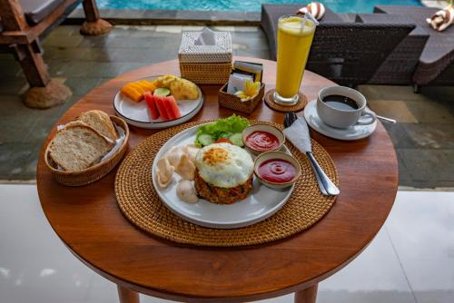 een tafel met een bord ontbijtproducten en een glas sinaasappelsap bij Tiara Villa Ubud by Dhananjaya Hospitality in Tampaksiring