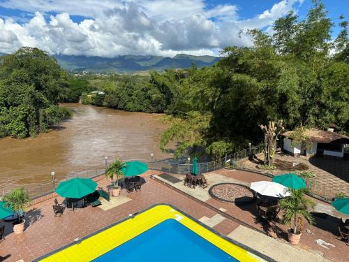 a swimming pool with tables and umbrellas next to a river at Hotel Cascada Cristalina in Melgar