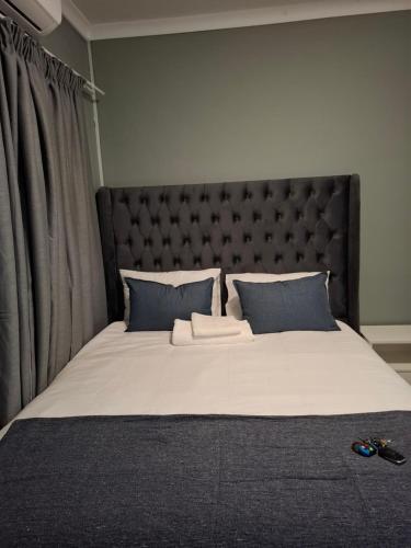a large bed with a black headboard and blue pillows at Cosy Cottage 1 in Francistown