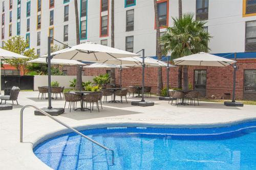 a pool with tables and chairs and umbrellas and a table and chairs at Hampton by Hilton Saltillo Zona Aeropuerto in Saltillo