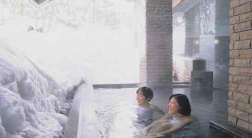 two people sitting in a hot tub with snow at Hotel de Premiere Minowa in Inawashiro