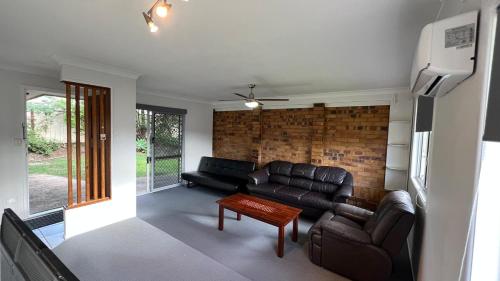 a living room with leather furniture and a brick wall at 3 Bed House free parking,Master with AC in Browns Plains