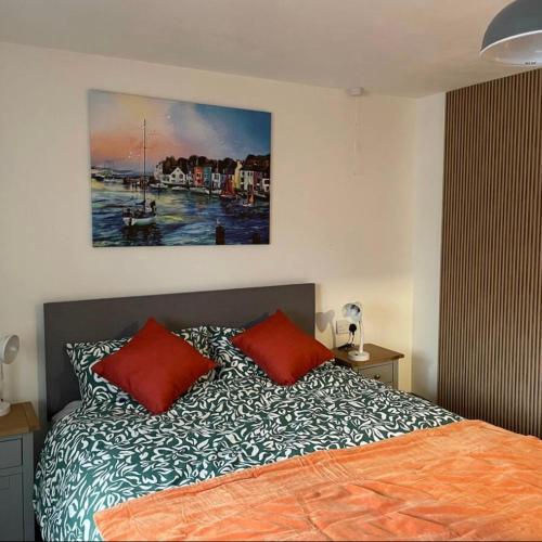 a bed with two red pillows and a painting on the wall at Corner Post Holiday Letting in Weymouth