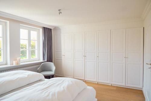 a white bedroom with white cabinets and a chair at Reethüs Keitum mit Kamin und Südgarten in direkter Wattnähe in Keitum