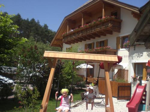 two children playing on a swing set in front of a house at Hotel Wieslhof in Collepietra