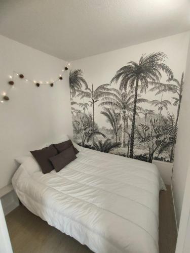 - une chambre avec un lit blanc et des palmiers sur le mur dans l'établissement Le doux viking appartement cosy balcon parking Caen Beaulieu, à Caen