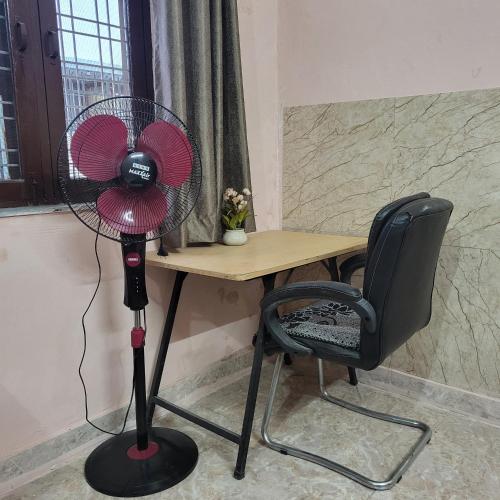 a fan sitting next to a desk with a chair at Peaceful Stay in Doon, Gateway to Mountains in Dehradun