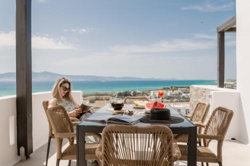 a woman sitting at a table on a balcony at Lithia Exclusive Villas in Plaka