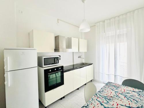 a white kitchen with a refrigerator and a microwave at Maredena - Comodo al centro e al Mare - Immobil Relax in Lido di Jesolo