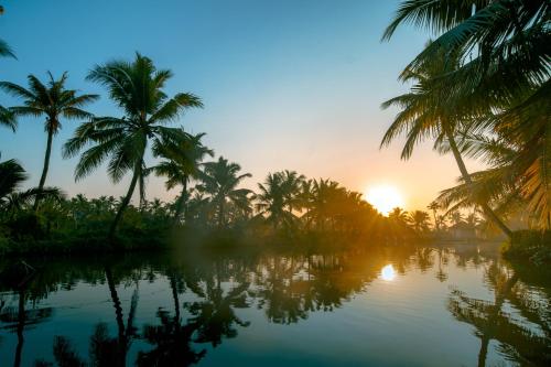 a view of a river with palm trees at sunset at Munroe Island Lake Resort in Kollam