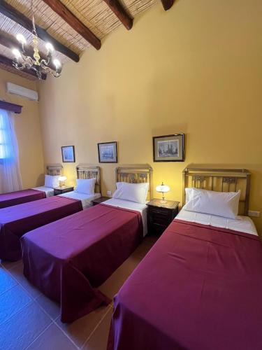 three beds in a room with purple sheets at La Sala Hotel Boutique in Tinogasta