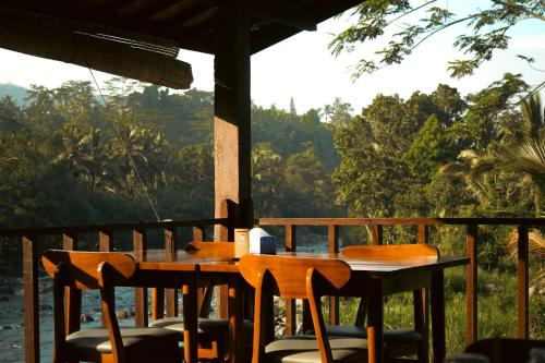 einen Tisch und Stühle auf einer Veranda mit Flussblick in der Unterkunft Villa Joglo tepi sungai in Sidemen
