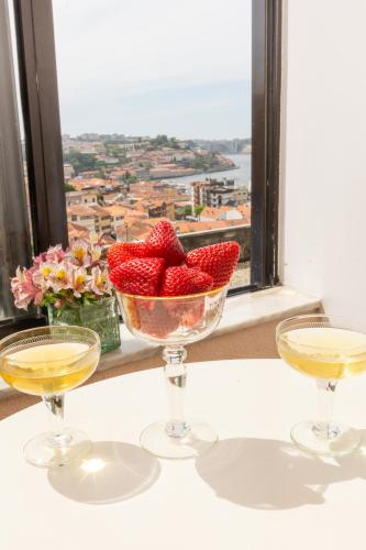 a bowl of strawberries and two glasses of wine at Jardim do Morro Places in Vila Nova de Gaia