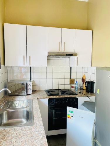 a kitchen with white cabinets and a stainless steel sink at Henry George Hotel in Pretoria
