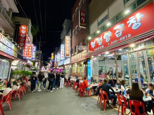 a city street with people sitting at tables in chairs at Beaver Stay, Bosu in Busan