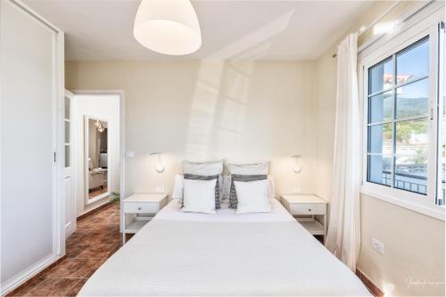 a white bedroom with a large bed with two windows at Casa Conrado, 2 bedroom modern oasis, good location in Puntallana